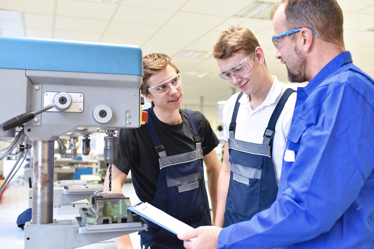 trainer and apprentice in technical vocational training at a drilling machine